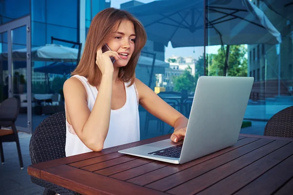 Mooi meisje die op laptop werkt en spreken op de telefoon in su — Stockfoto