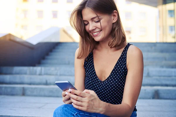 Junge lächelnde Frau sitzt draußen und tippt ein Meesage auf Mob — Stockfoto