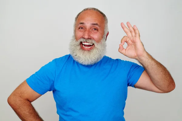 Alter Mann mit weißem Bart und breitem Lächeln, der eine freundliche Geste zeigt — Stockfoto