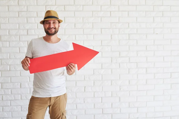 Smiling man is standing and holding big red arrow — Stock Photo, Image