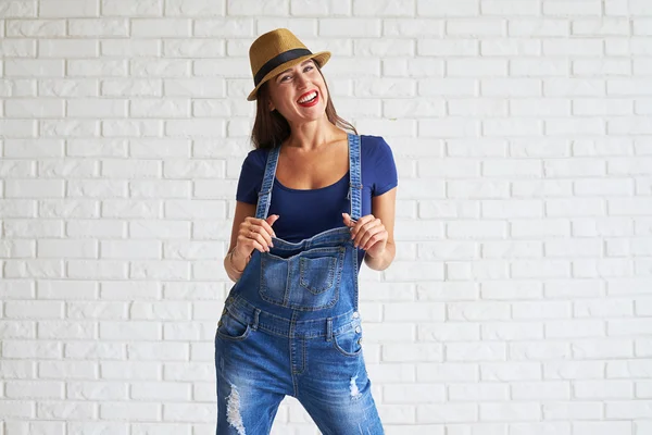 Mulher sorridente usar chapéu de palha e de pé contra uma parede branca — Fotografia de Stock