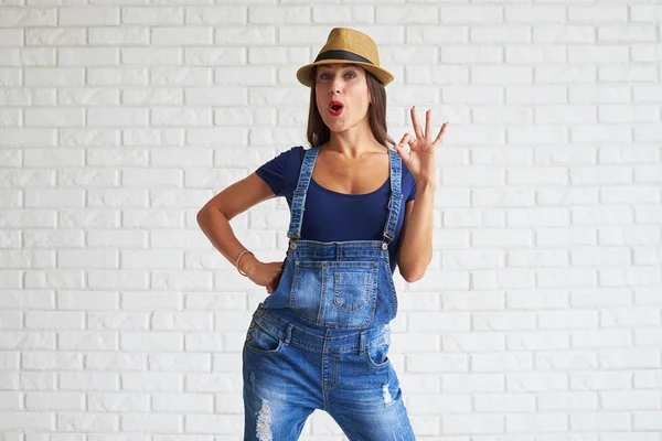 Mulher usar chapéu de palha e mostrando ok contra uma parede branca — Fotografia de Stock