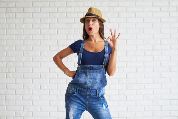 Donna indossare cappello di paglia e mostrando ok contro un muro bianco — Foto Stock