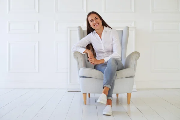 Mujer joven sentada en un sillón moderno relajándose en su habitación —  Fotos de Stock