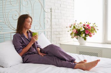 Bir fincan çay looki ile beyaz yatakta güzel kadın Portresi