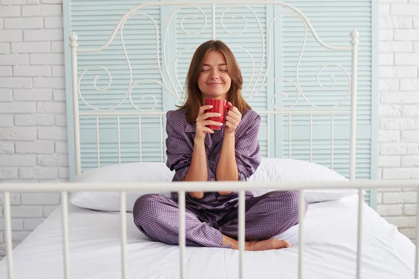 Attractive woman in pajamas on bed enjoying the smell of her mor — Stock Photo, Image