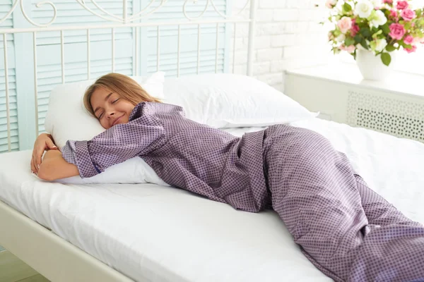Attraktive junge Frau in Satin-Pyjama schlafen auf dem Bett mit wh — Stockfoto