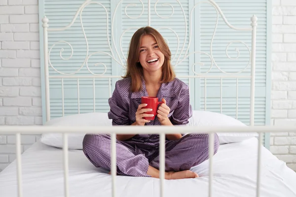 Schöne braunhaarige Frau sitzt auf dem Bett mit einer Tasse Kaffee — Stockfoto