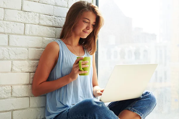 Delighted smiling girl working on her laptop while sitting on th — Stock Photo, Image