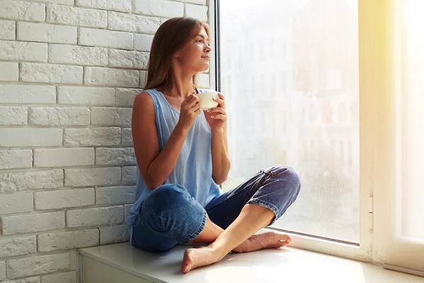 Blij en geïnspireerd jonge vrouw die door het raam kijkt — Stockfoto