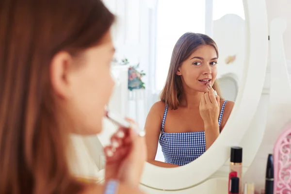 Reflejo de una jovencita mirando al espejo y sosteniendo un labio — Foto de Stock