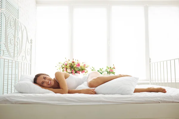 Сексуальна дівчина в білій білизні лежить грайливо на ліжку з однією ногою — стокове фото