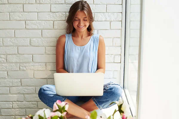 Ragazza elegante con computer portatile seduto sul davanzale della finestra con le croci gamba — Foto Stock