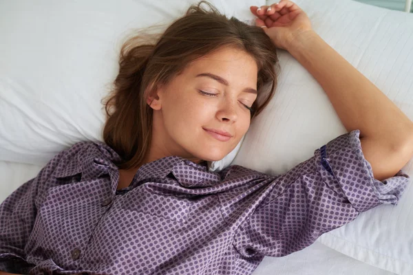 Young woman in pajamas sleeping peacefully on her back with one — ストック写真