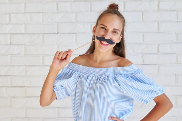 Fröhliche junge stilvolle Mädchen posiert mit einem Papierschnurrbart auf sti — Stockfoto