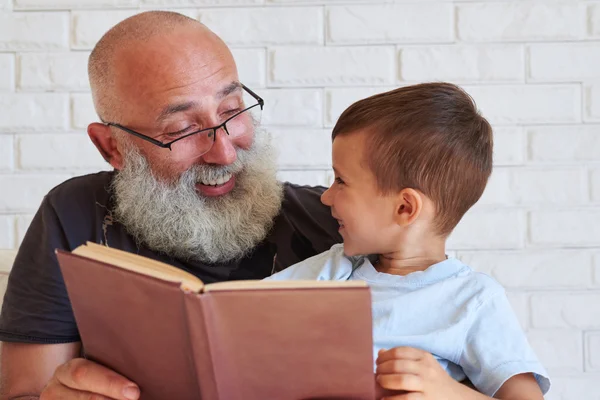 Крупный план пожилого мужчины и маленького мальчика с книгой, глядя на каждый о — стоковое фото