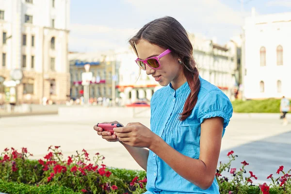 Gros plan de jolie adolescente en lunettes de soleil roses utilisant son smartph — Photo