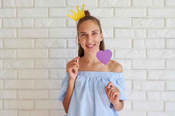 Chica bonita positiva sonriendo mientras sostiene una corona de papel y una h — Foto de Stock