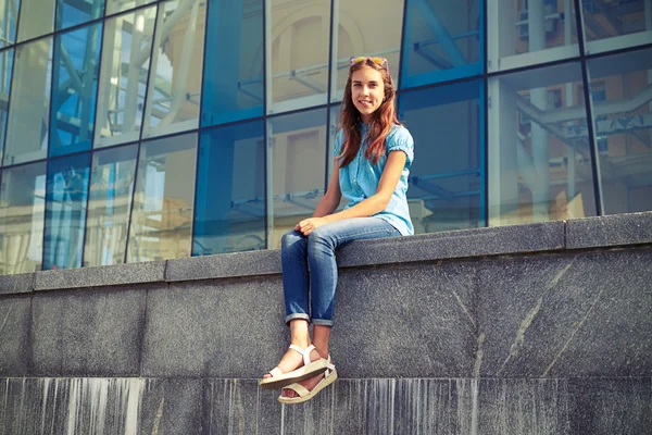 Štíhlá mladá dívka v příležitostných šatech, která sedí proti obchodnímu centu — Stock fotografie