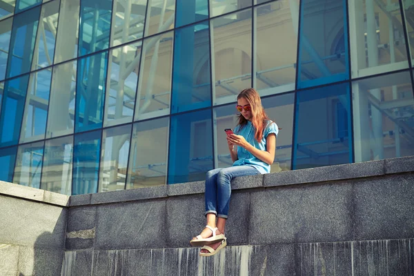 Trendy stijlvol meisje met behulp van mobiele telefoon in het centrum — Stockfoto