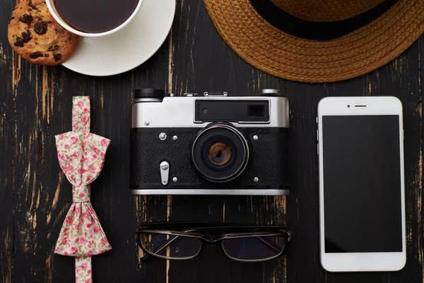 Wooden table with hat, old-fashioned camera, eyeglasses, floral — Stock fotografie