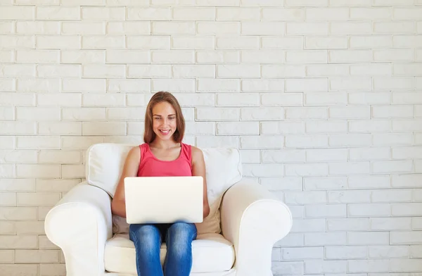 Mooie tiener meisje met geopende laptop in witte fauteuil tegen — Stockfoto