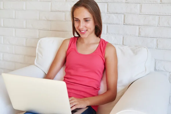 Menina bonita trabalhando no laptop sentado em poltrona aconchegante — Fotografia de Stock