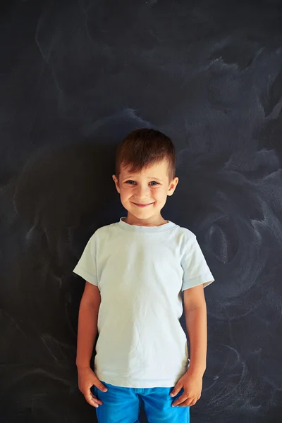 Mignon petit garçon souriant debout contre le tableau noir de l'école — Photo