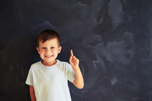 Retrato de un niño pequeño mostrando el dedo índice contra la escuela blackboa — Foto de Stock