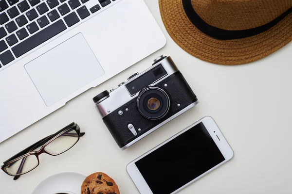 Bílý povrch s klobouk, brýle, notebook, fotoaparát smartphone — Stock fotografie