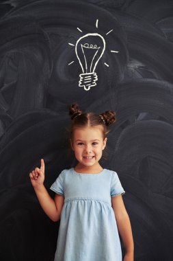 Gülümseyen küçük kız ampul çizim tebeşir karşı ayakta