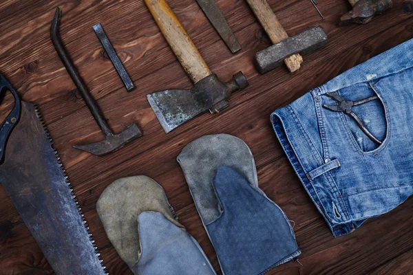 Top view of worn tools kit and denim jeans with gloves over wood
