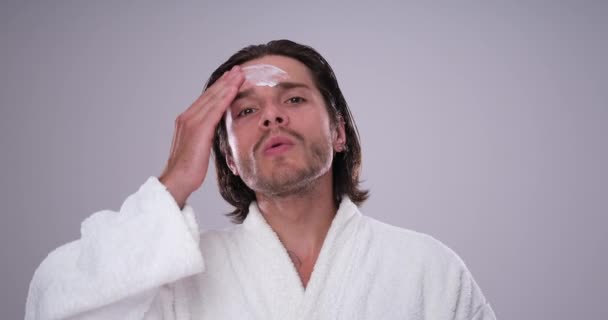 Hombre en albornoz aplicando crema en la cara — Vídeos de Stock