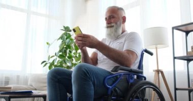 Tekerlekli sandalyede oturan engelli yaşlı adam cep telefonu kullanıyor.