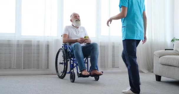 Женщина-медсестра заботится о пожилом мужчине-инвалиде с помощью мобильного телефона на инвалидной коляске — стоковое видео