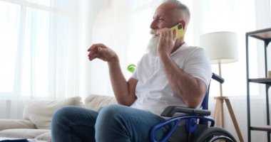 Tekerlekli sandalyede oturan engelli yaşlı adam cep telefonuyla konuşuyor.