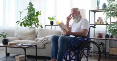 Tekerlekli sandalyede kitap okuyan engelli kıdemli adam.