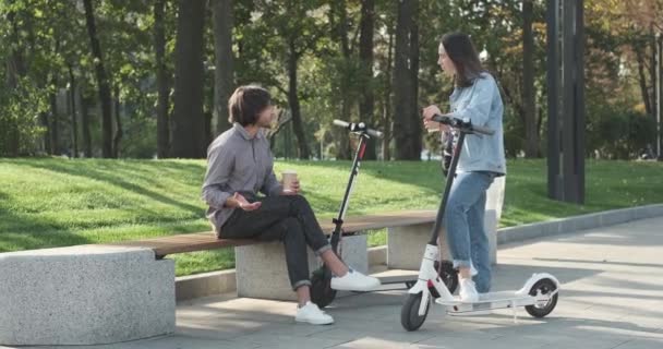 Пара розмовляє з чашкою кави та електронним скутером у парку — стокове відео