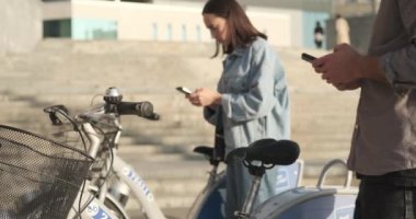 E-scooter sürmek üzere olan bir adam ve kadın cep telefonu kullanıyor.