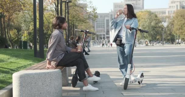Paar gesprekken met koffiekop en e scooter in het park — Stockvideo