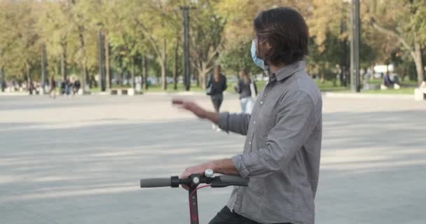 Pareja con máscara facial protectora saludándose y montando scooter eléctrico — Vídeos de Stock