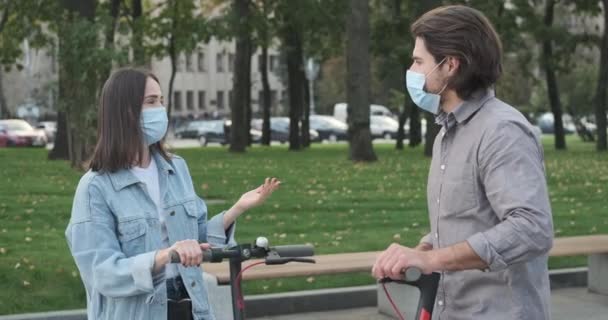 Amici che indossano una maschera protettiva e parlano appoggiati a scooter elettrici — Video Stock