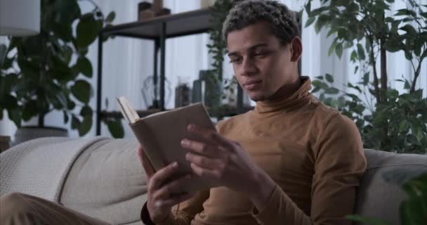 Hombre leyendo un libro en el sofá en casa — Vídeo de stock