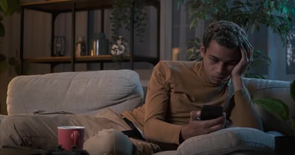 Hombre estresado usando el teléfono móvil y durmiendo en el sofá por la noche — Vídeo de stock