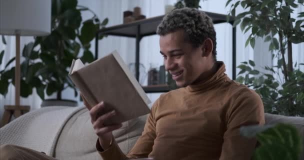 Mies lukee kirjaa sohvalla kotona — kuvapankkivideo
