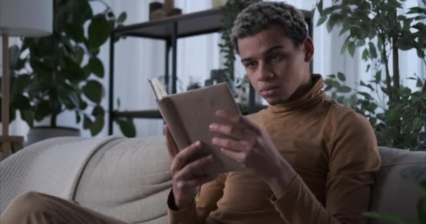 Hombre leyendo un libro y tomando café en el sofá en casa — Vídeo de stock