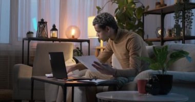 Bilgisayarı kullanan ve evdeki belgeleri analiz eden bir adam.