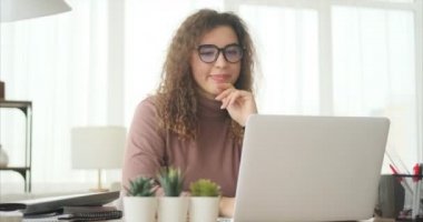 Dizüstü bilgisayarda çalışan ve ofiste kahve içen bir kadın.