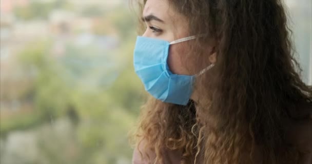Kvinna bär ansiktsmask och tittar ut genom fönstret — Stockvideo