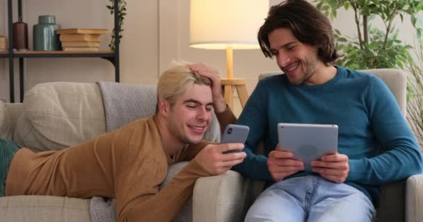Gay couple using mobile phone and digital tablet at home — Stock Video